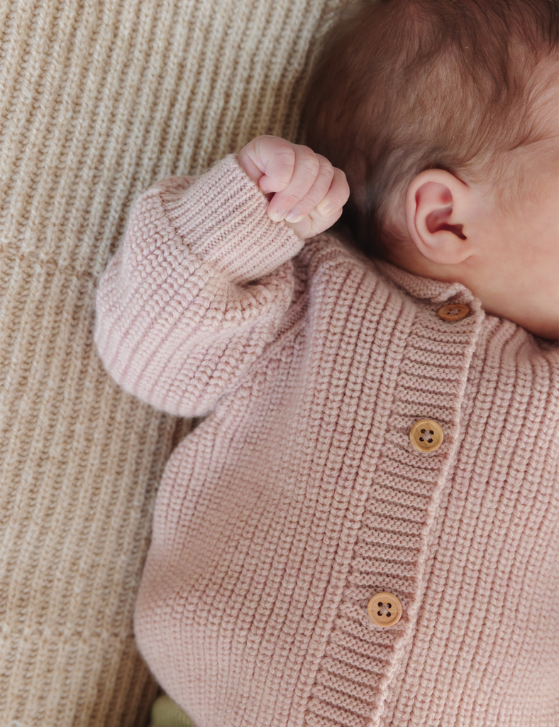 Baby wearing a knitted pink sweater with button details on a soft background