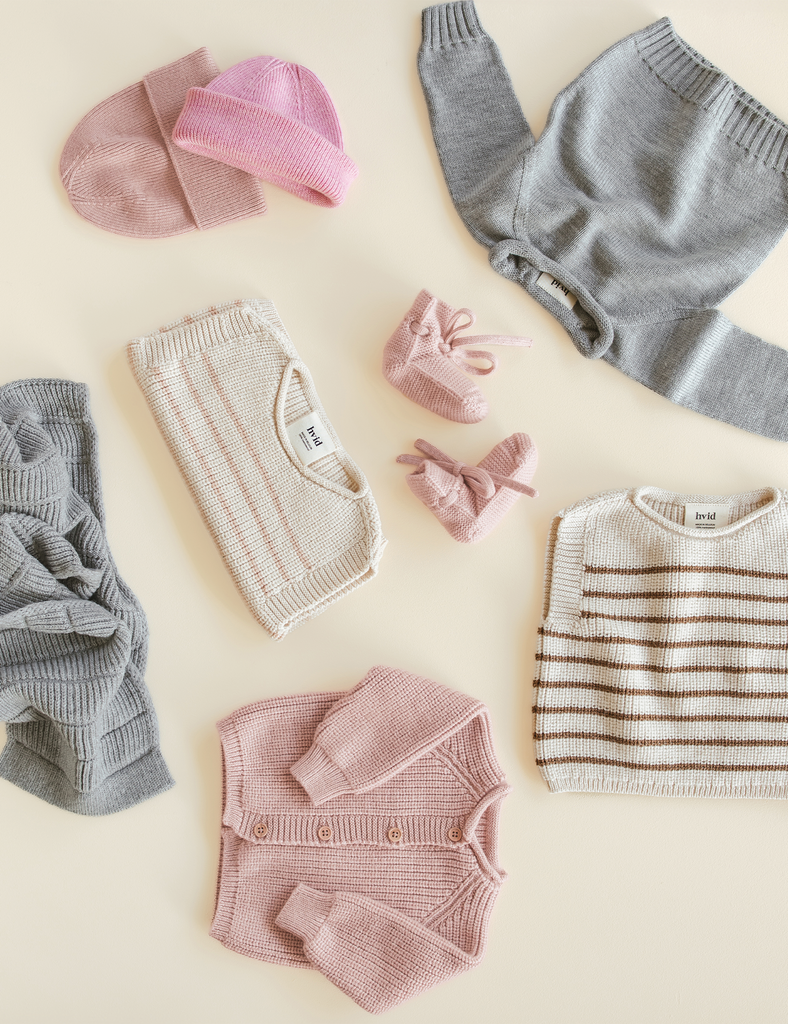 Collection of baby clothing including sweaters, a hat, and a cardigan on a light background