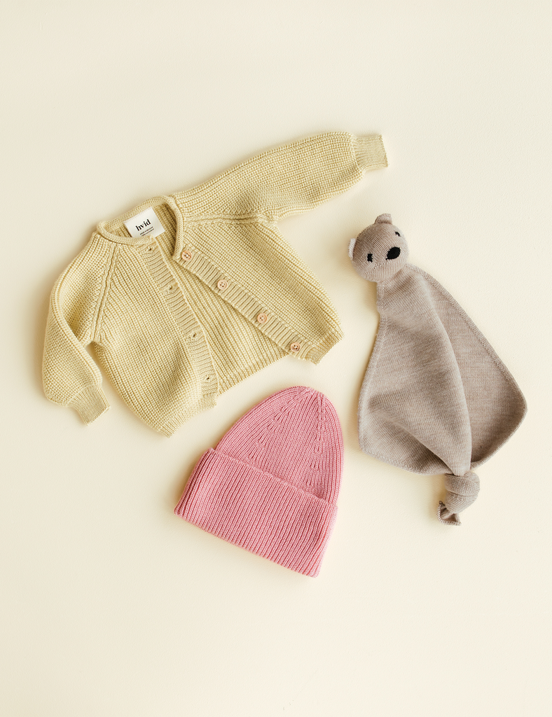 Baby sweater, pink beanie, and gray comfort blanket on a beige background