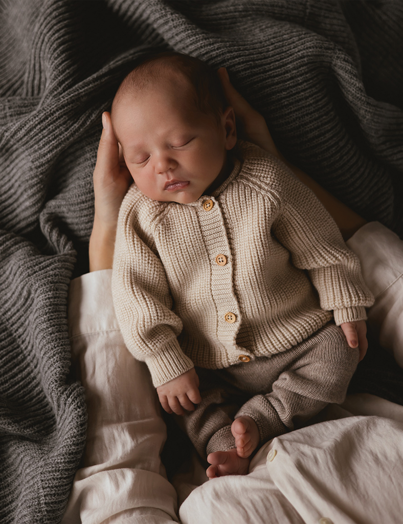 Baby in a beige outfit being held.