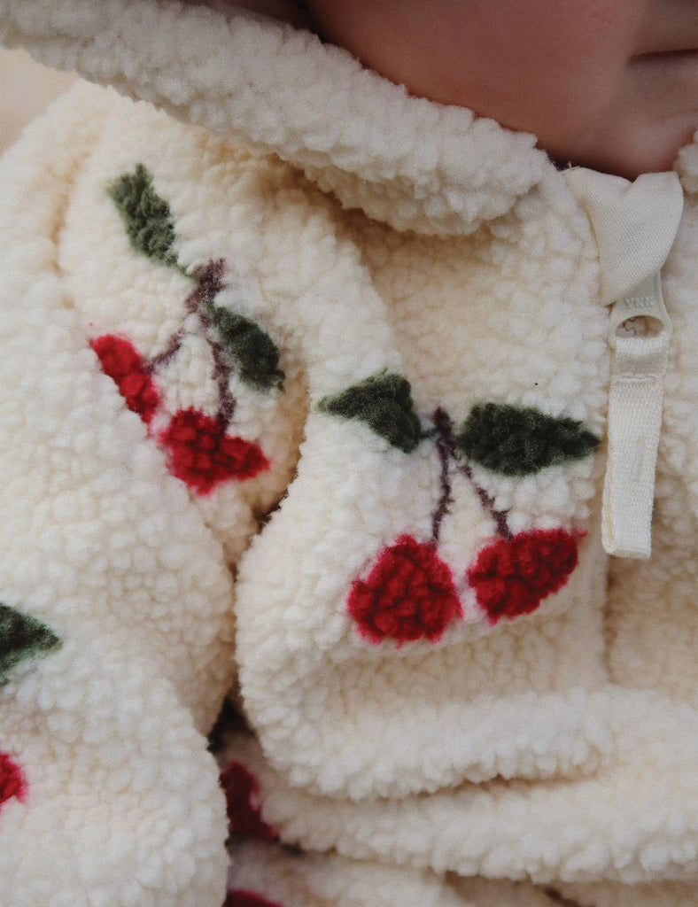 Image of  a baby wearing a hooded fleece bodysuit with an allover cherry print.