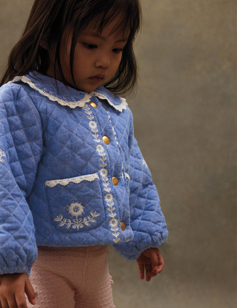 Child wearing a blue quilted jacket with floral embroidery on a neutral background