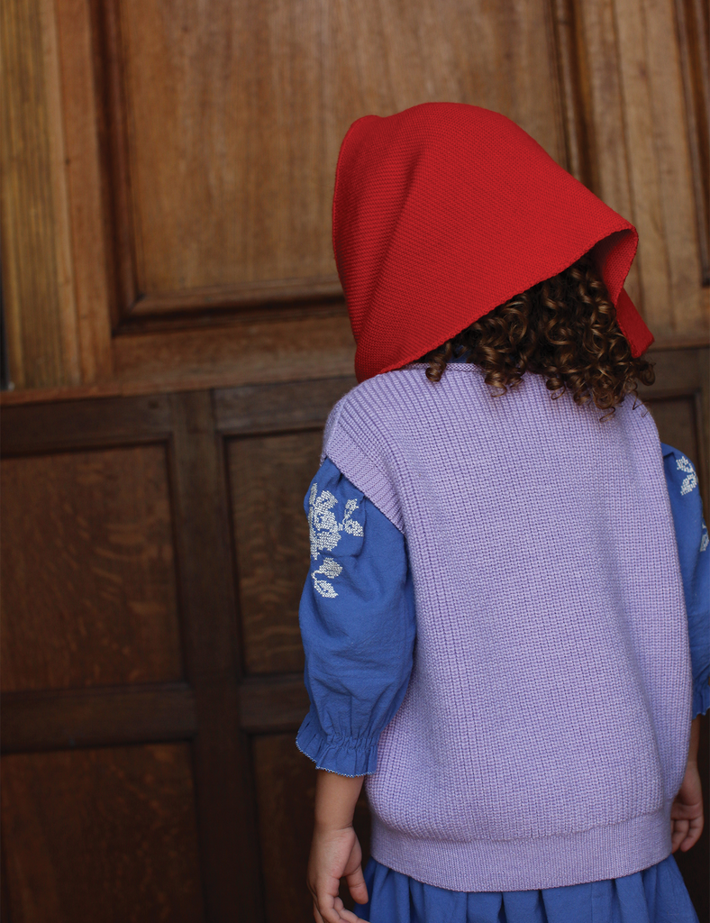 Person wearing a red hooded garment with a wooden panel background