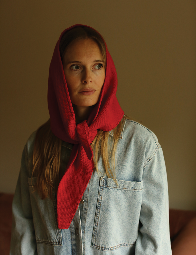 Woman wearing a red headscarf and light blue denim jacket against a plain background