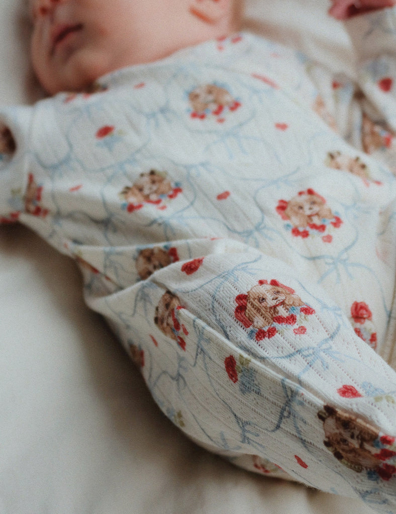 Newborn baby wearing a puppy pattern kimono style onesie on a soft ground