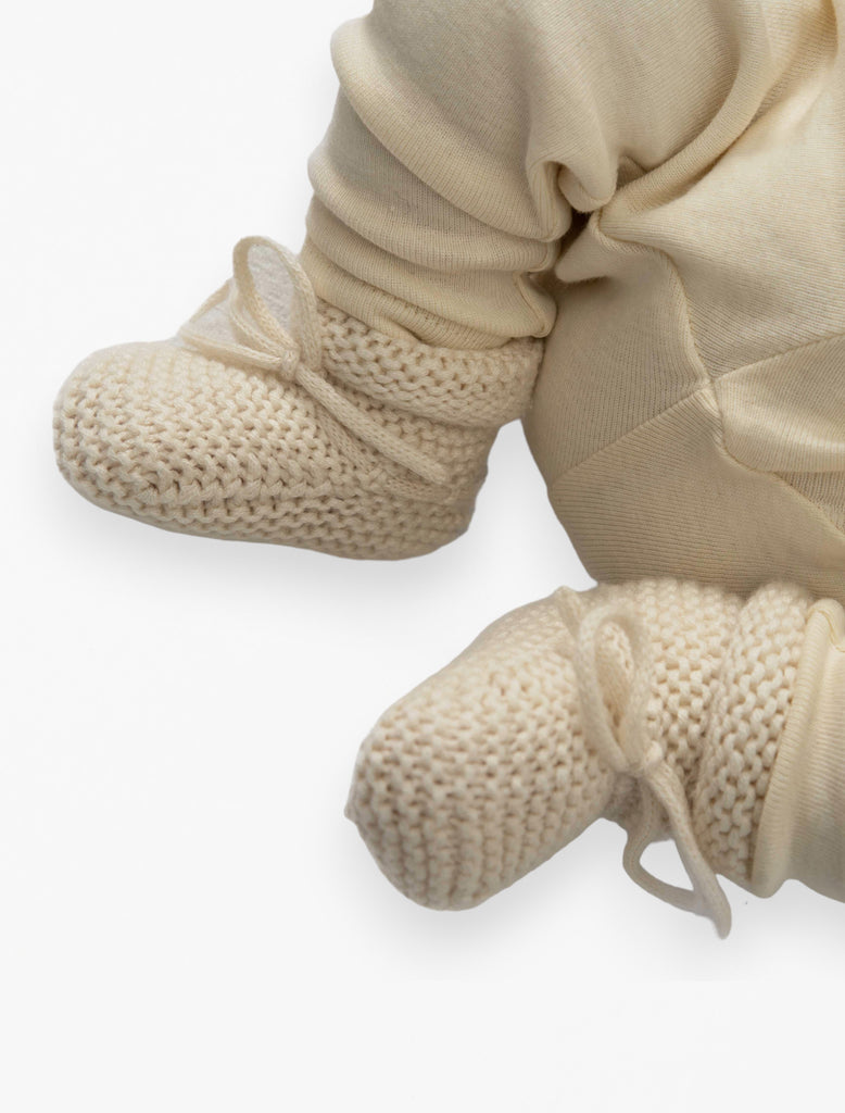 Baby wearing knitted booties in buttercream.