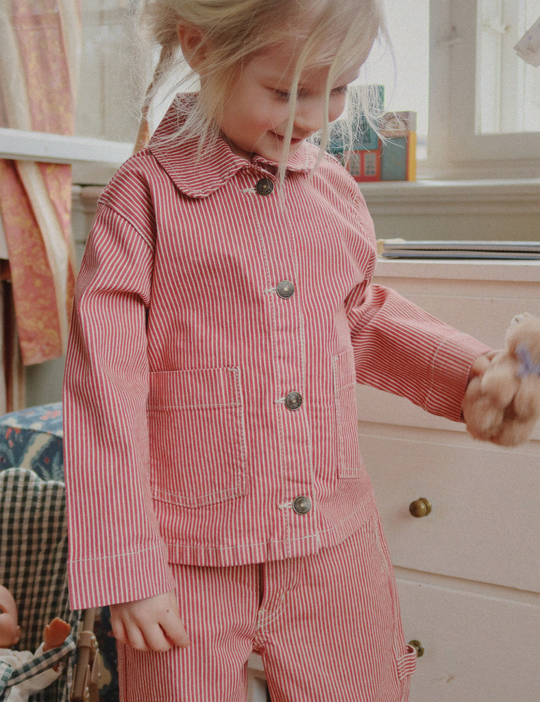 Child wearing a red and white striped outfit holding a teddy bear indoors.