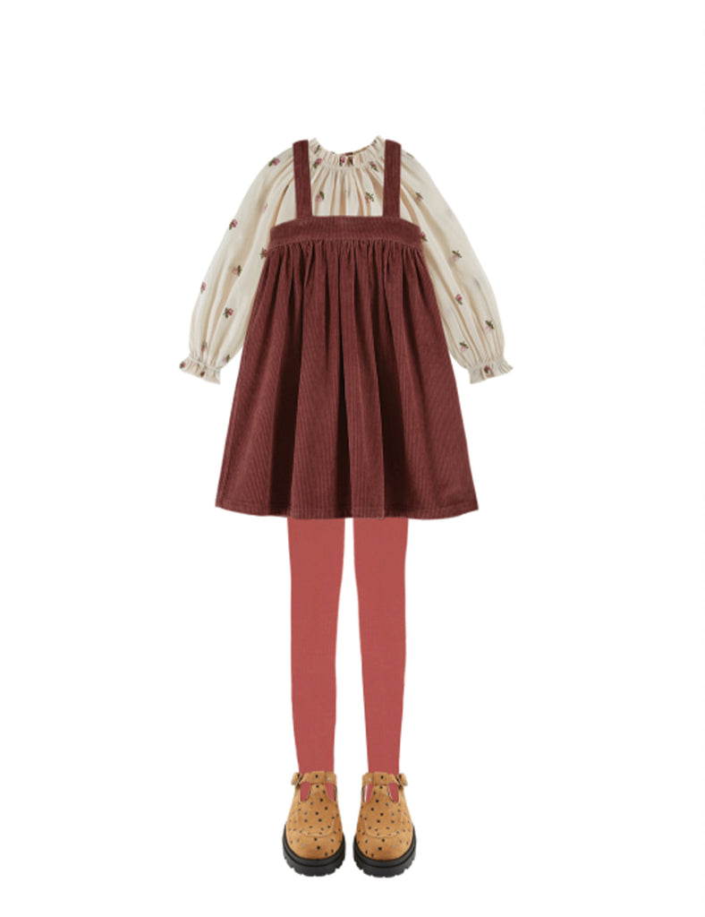 Brown pinafore dress with beige blouse and red tights on a white background