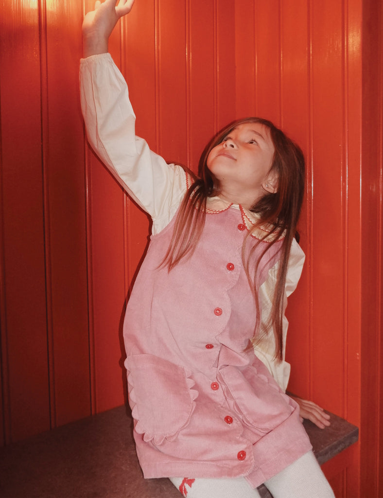 Child wearing a pink dress against a red wall