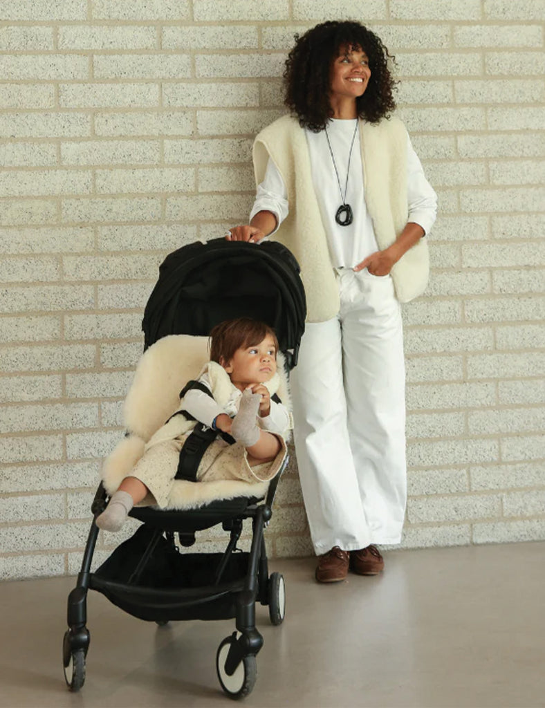 Woman pushing a stroller with a child inside against a brick wall.