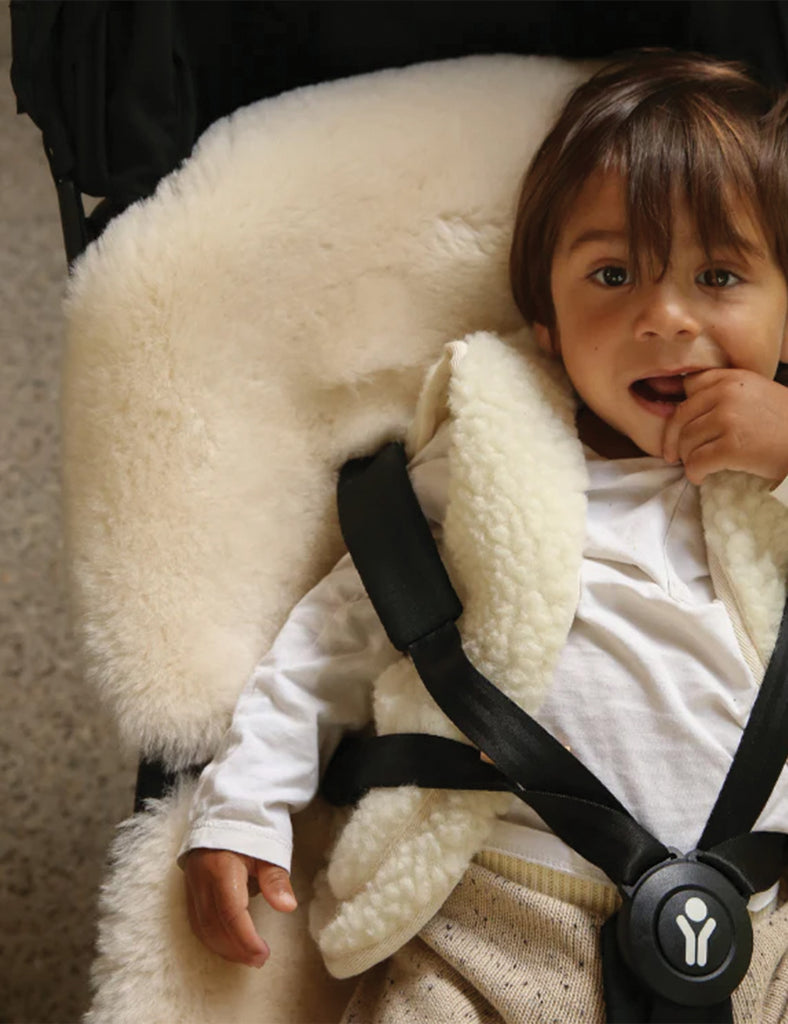 Child in a carrier with a white fluffy cover and black straps