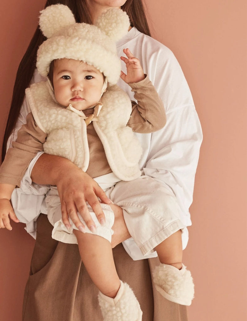 Child in a fluffy outfit being held by an adult against a pink background