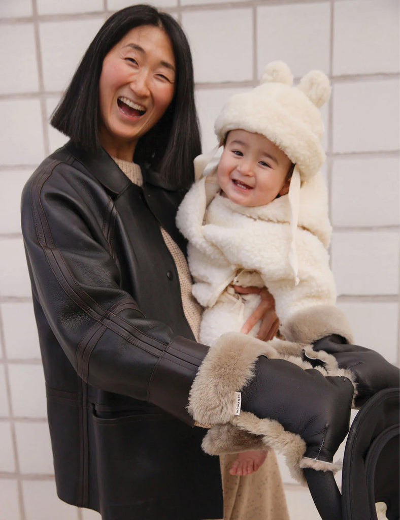 Woman holding a baby wrapped in a white blanket with bear ears against a tiled wall.