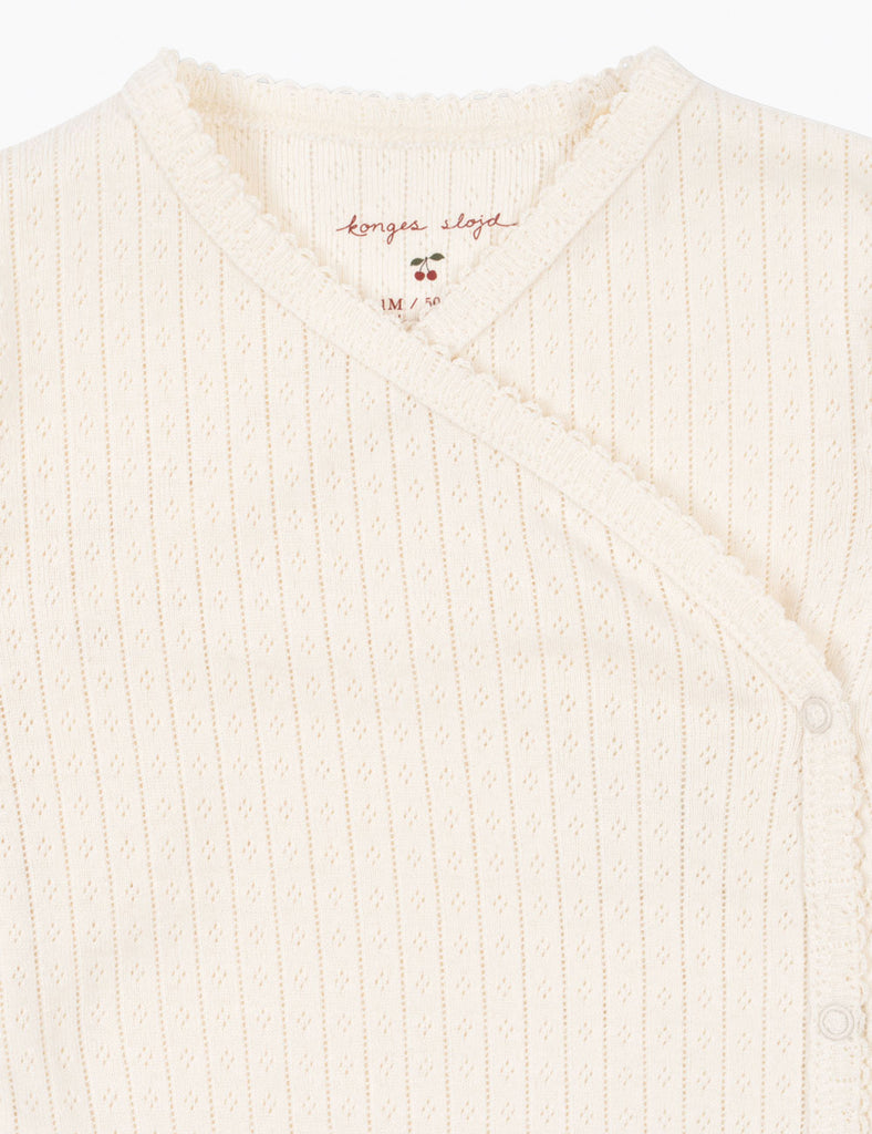 Close-up of a cream-colored ribbed sweater with a brand logo on a white background