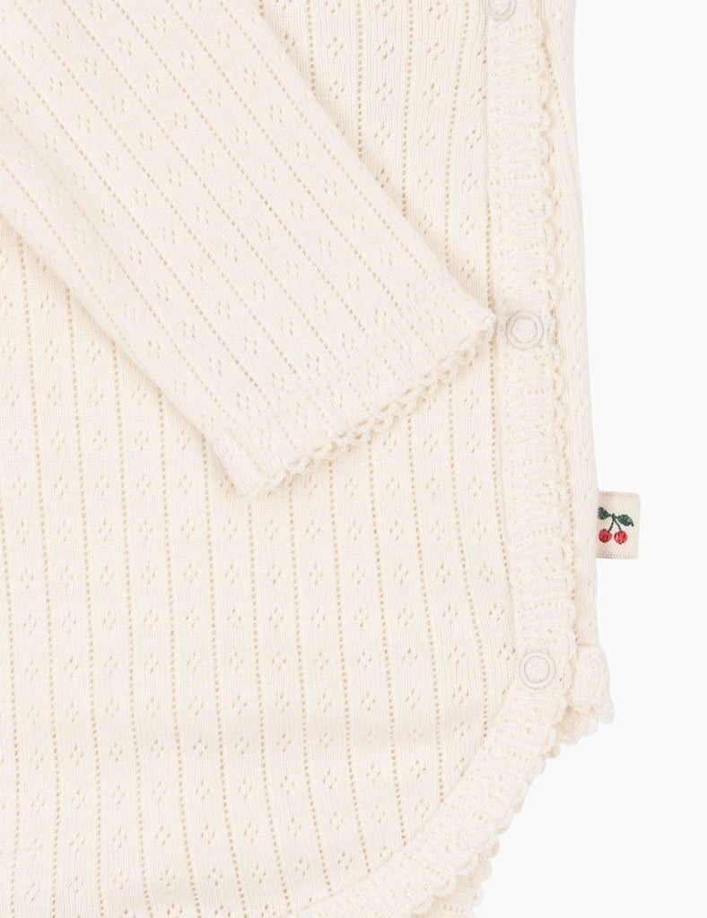 Close-up of a cream-colored knitted garment with a brand tag featuring red cherries.