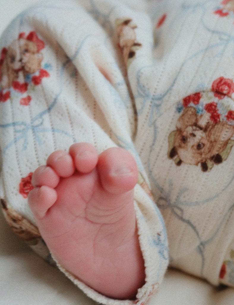 Baby foot peeking out from puppy-patterned pants while laying on a bed