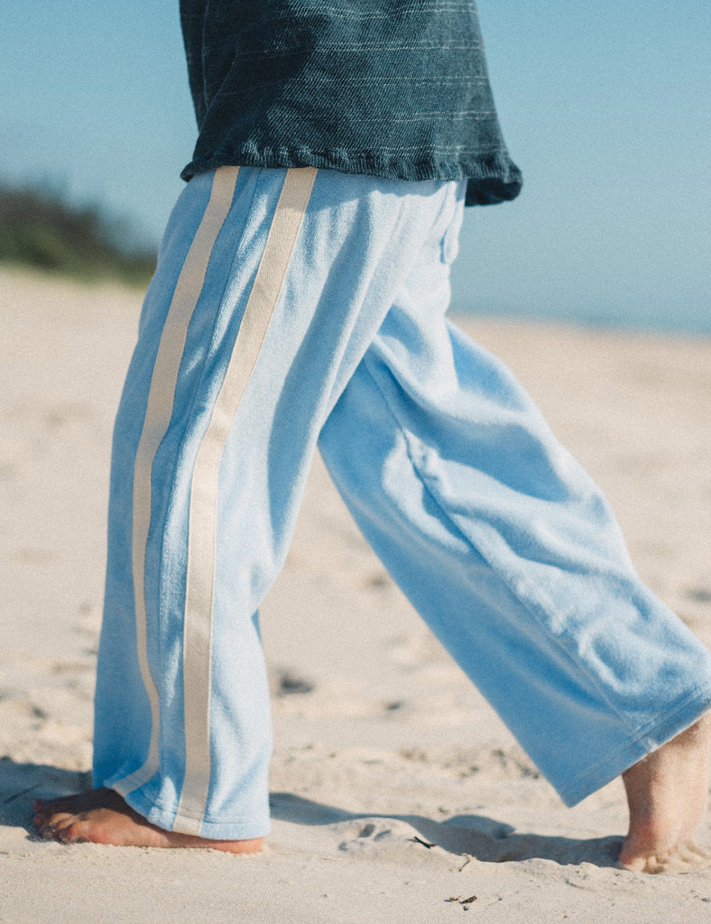 Person wearing light blue pants with white stripes on a sandy beach.