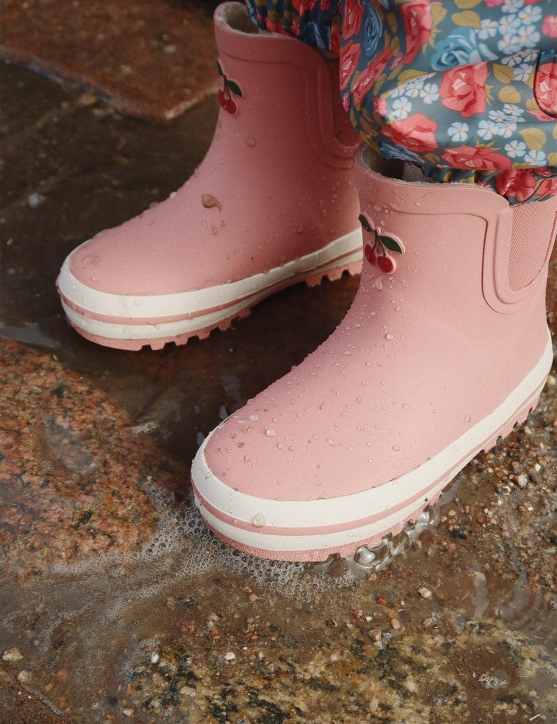 Pink rain boots with white soles on a wet pavement