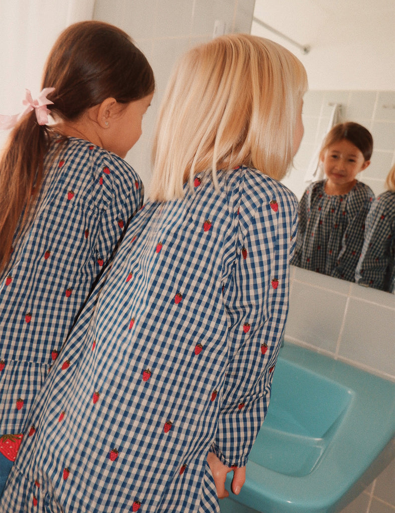 Two children in matching blue checkered pajamas standing in front of a mirror.
