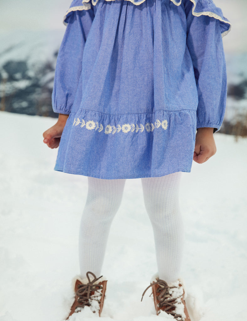 Child wearing a blue dress with floral embroidery in the snow