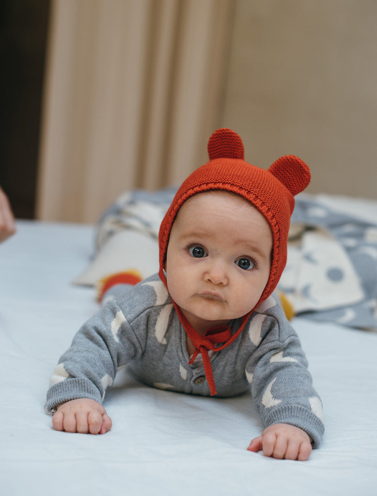Orion knitted baby bonnet in tortoise red lifestyle image.