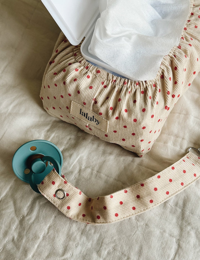 Baby pacifier with strap and polka dot pouch on a light background