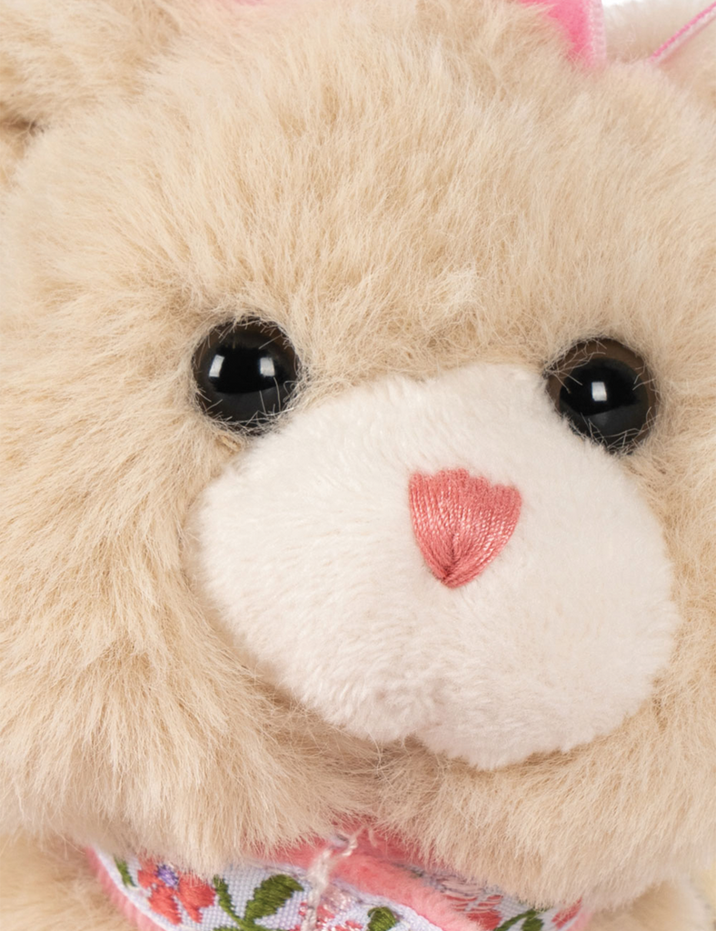 Close-up of a teddy bear with a pink bow and floral pattern on its chest.
