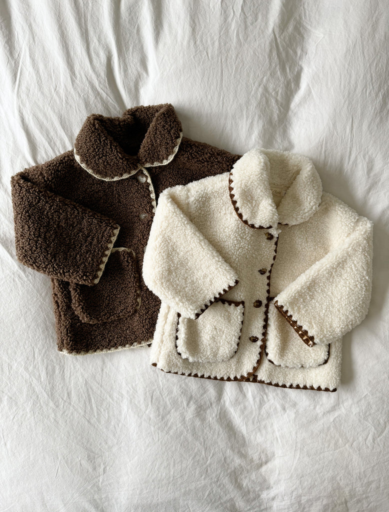 An image of both Paddy Jackets in brown and winter white. The jackets are laying flat on a whtie duvet cover.