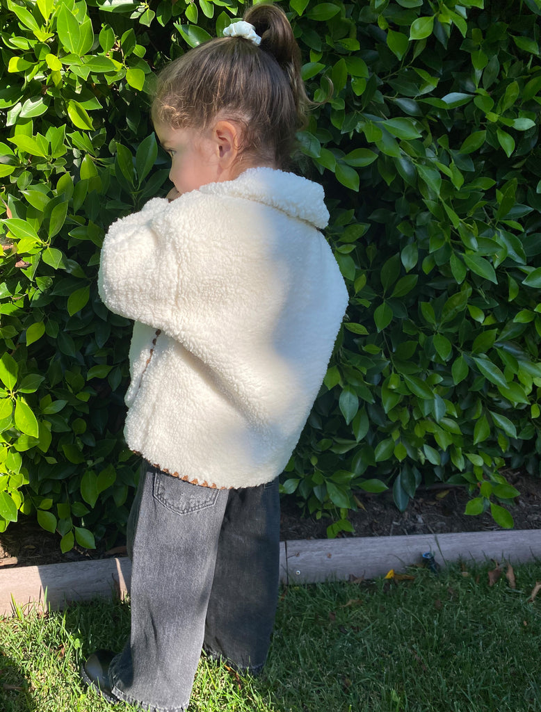 Sloane wears the Paddy Jacket in WInter White. She is outside next to a green hedge.