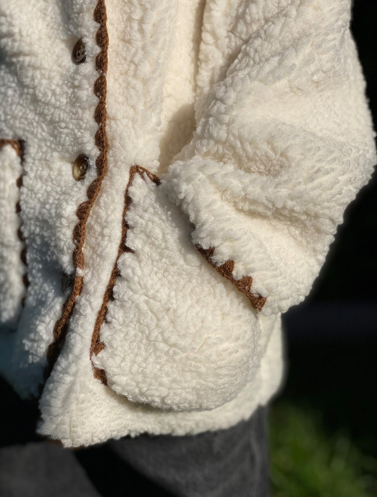 Sloane wears the Paddy Jacket in WInter White. She is outside next to a green hedge.