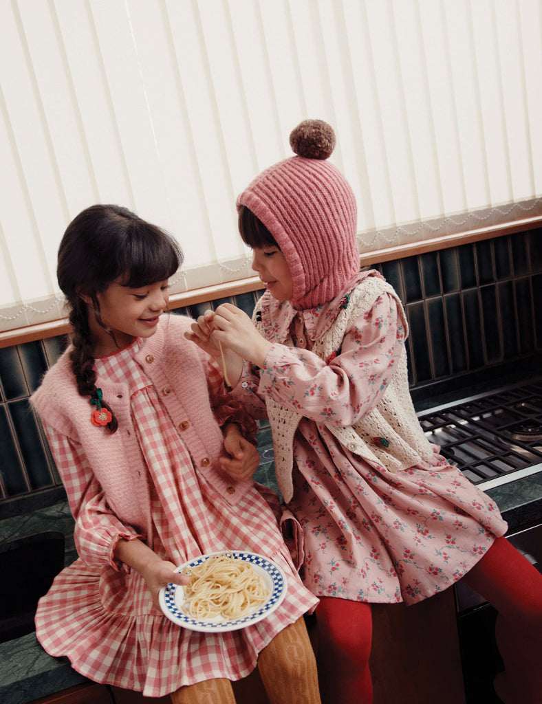 Two children in pink and red outfits sitting on a bench, one holding a plate of food.