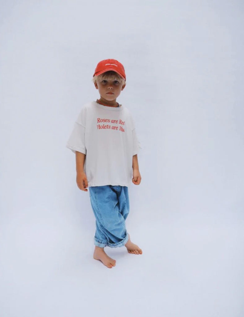 Child wearing a white t-shirt with text and blue pants on a light gray background