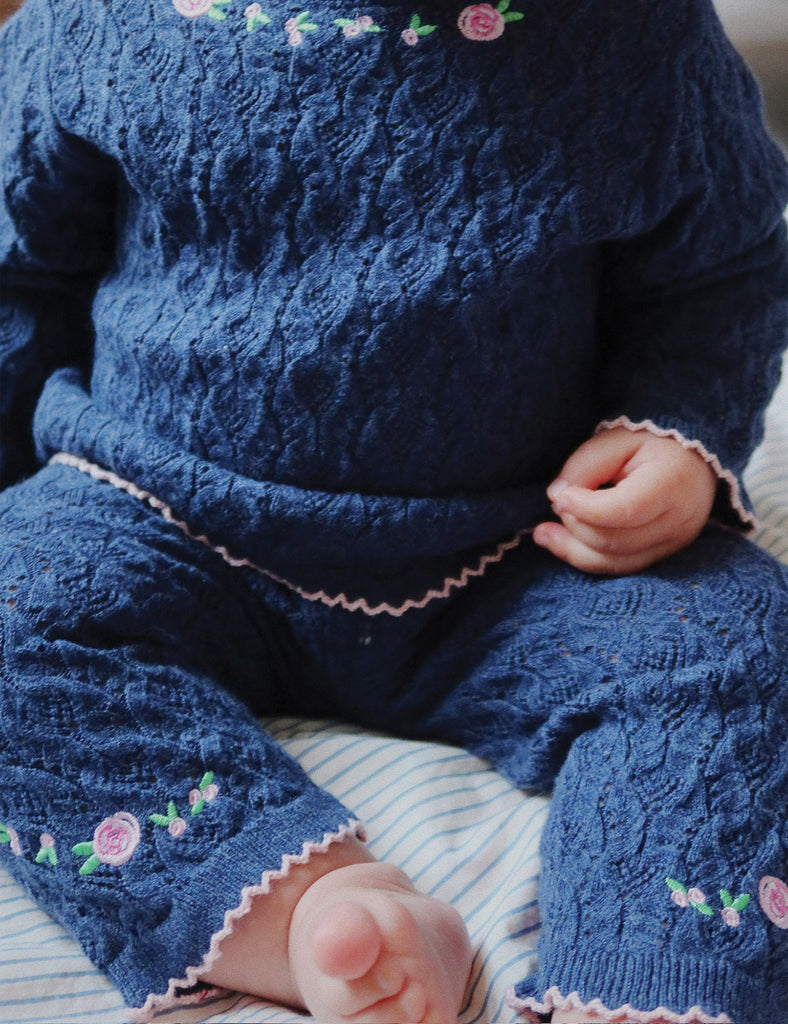 Close-up of a child wearing a blue knitted outfit with floral patterns.