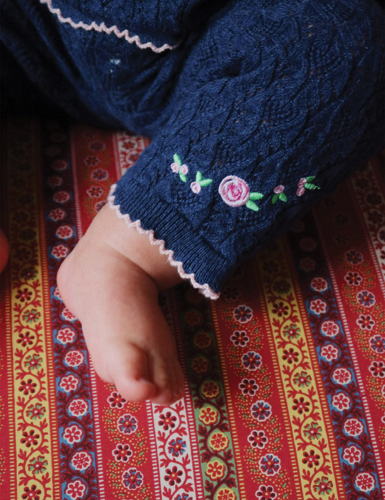Navy blue sweater with floral embroidery on a colorful patterned fabric background