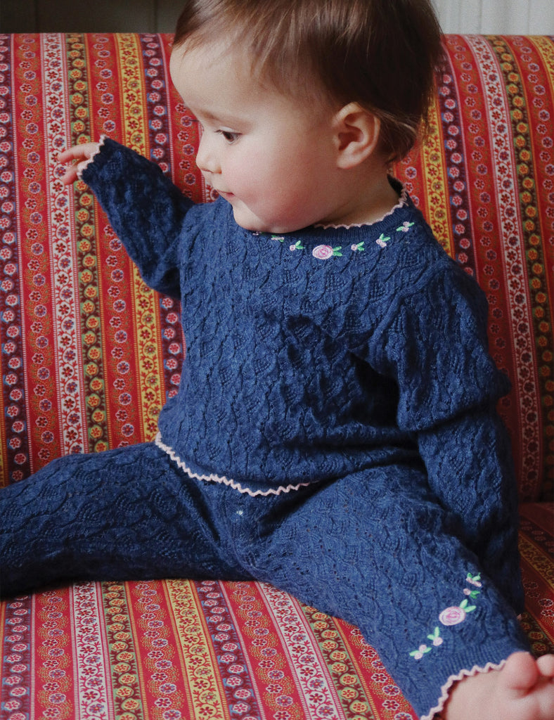 Child wearing a blue knitted outfit sitting on a colorful patterned couch.