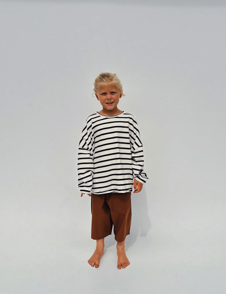 Child wearing a black and white striped shirt and brown pants on a plain background