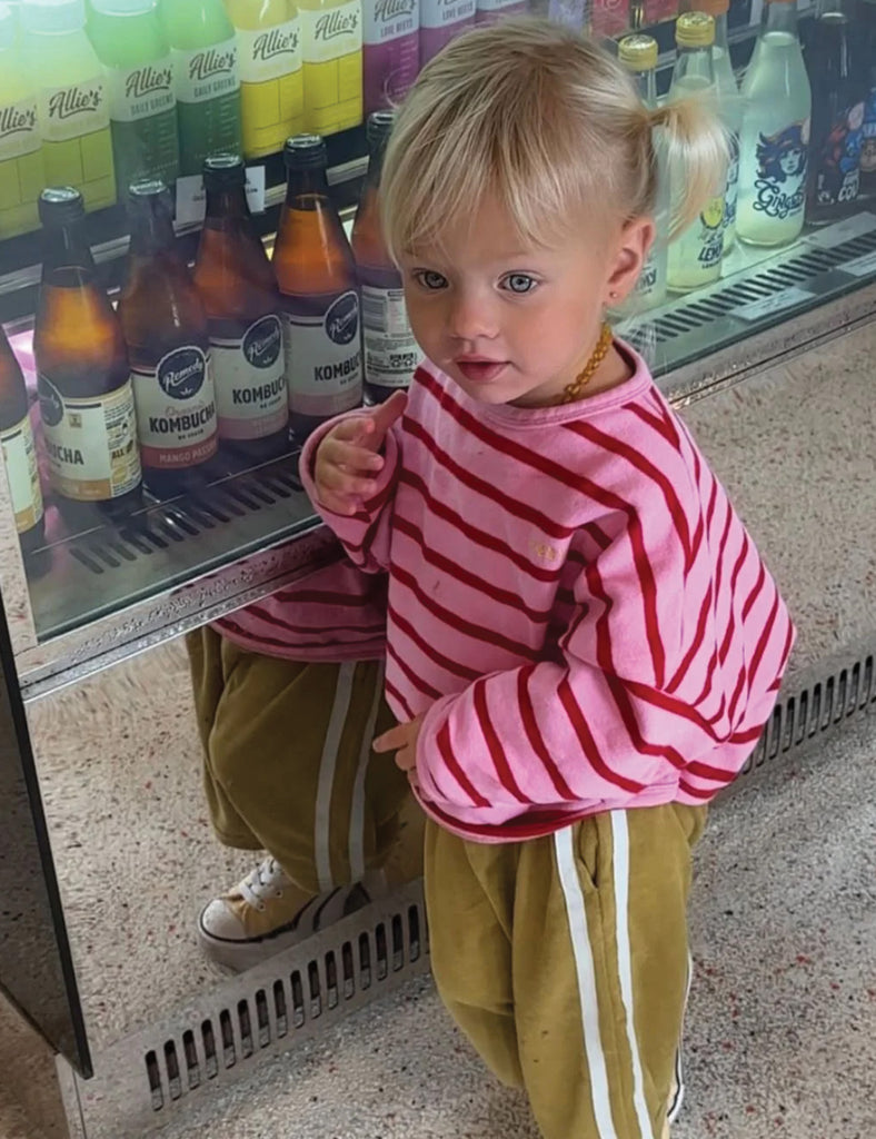 Child in a pink and red striped shirt standing in front of a store shelf with drinks.