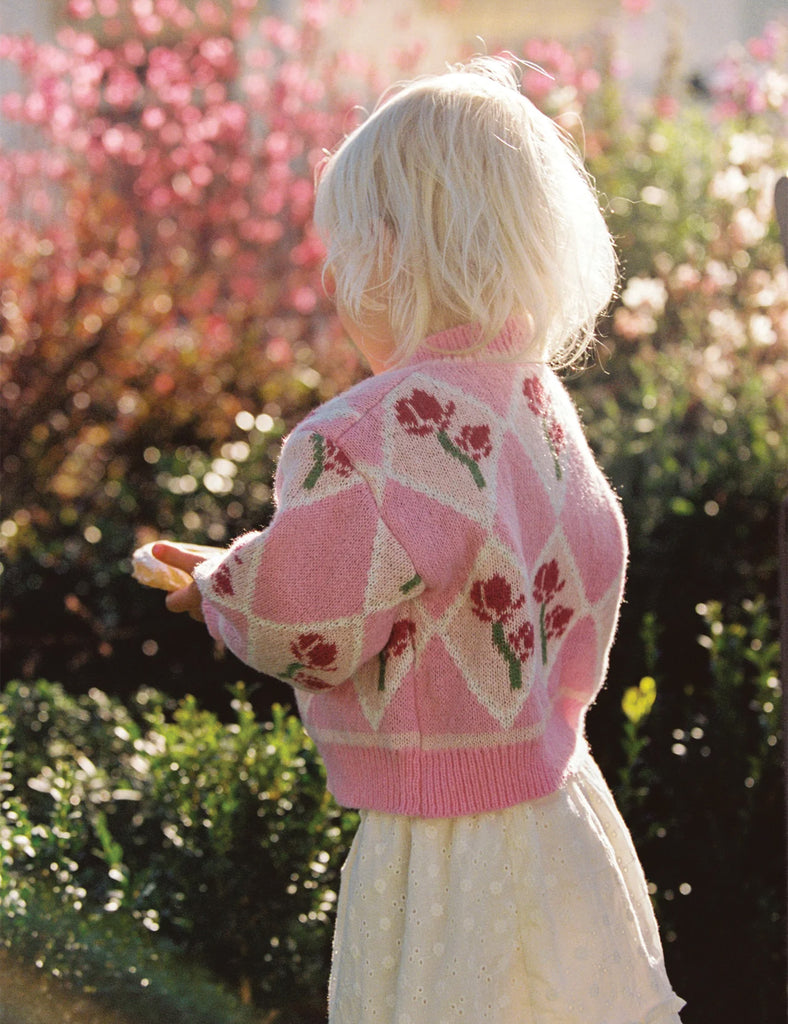 Child wearing a pink and white patterned cardigan in a garden setting