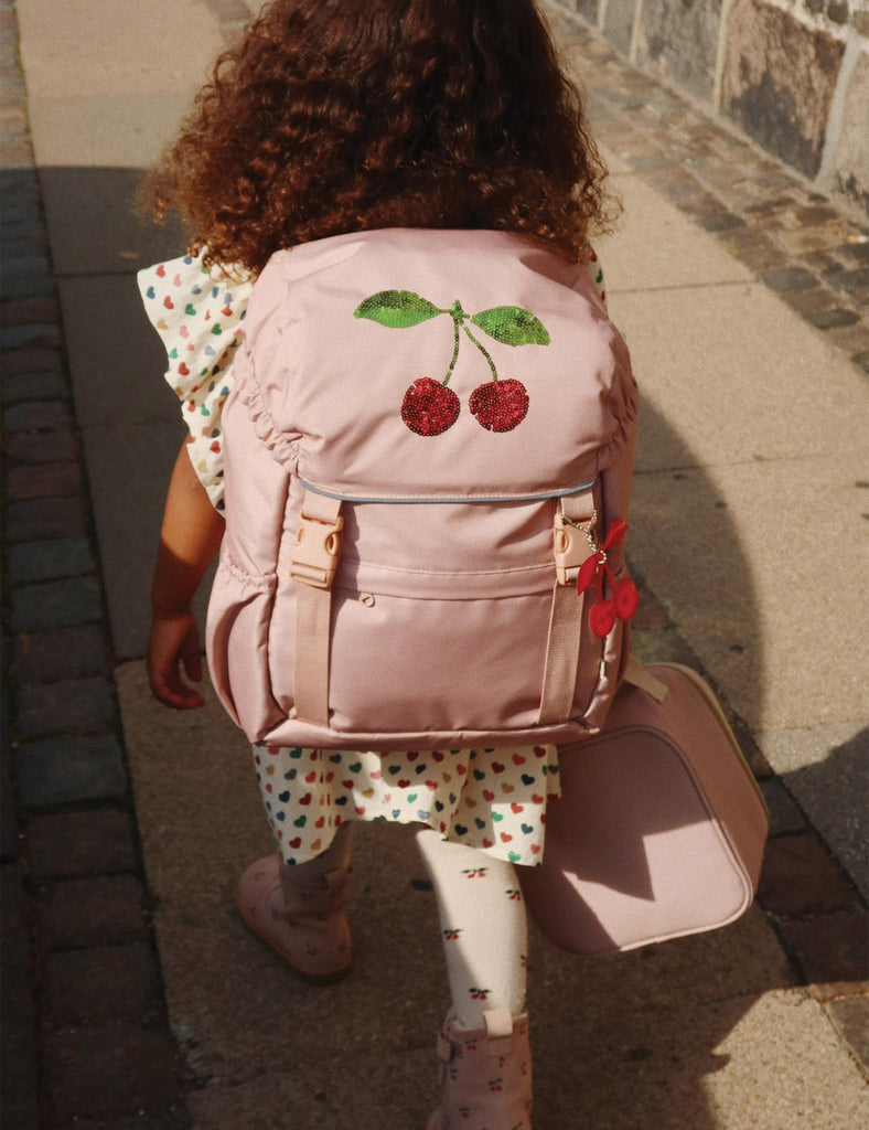 Child walking on a sidewalk with a pink backpack featuring cherry design