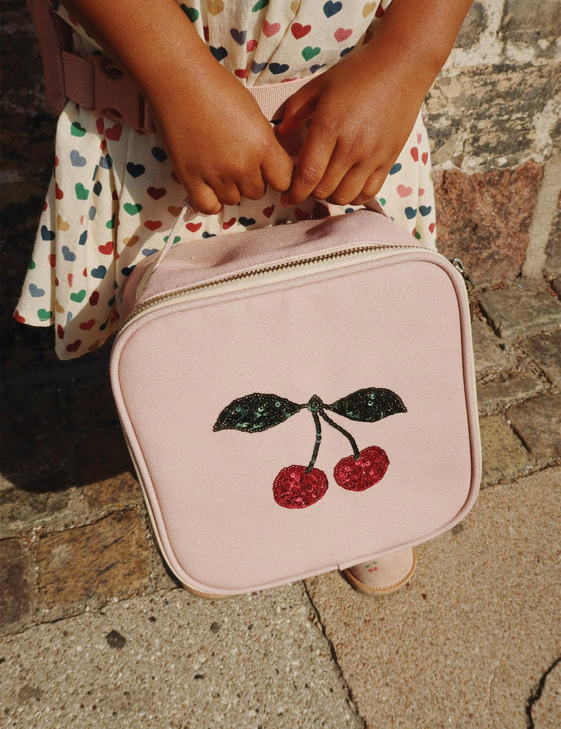 Pink bag with cherry design held by a person in a patterned dress on a stone pavement.