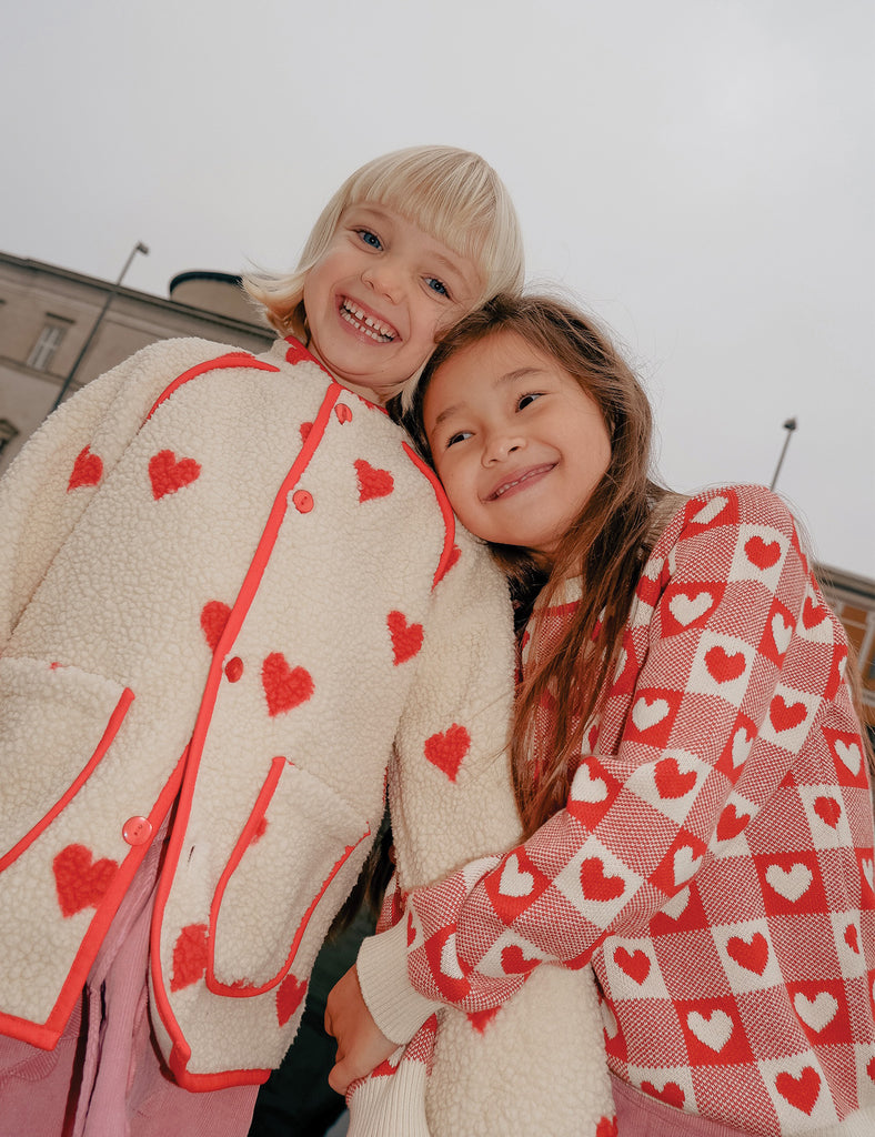 Two children wearing jackets with red heart patterns, standing close together.