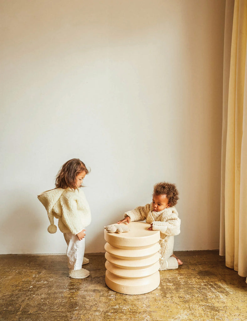 Two children playing with a stack of wooden rings in a minimalistic room.