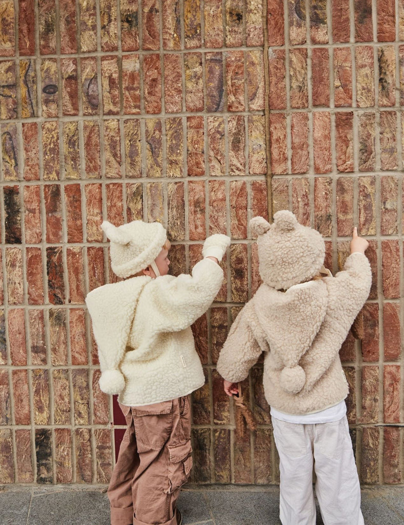 Two children wearing fluffy hoodies against a textured wall.