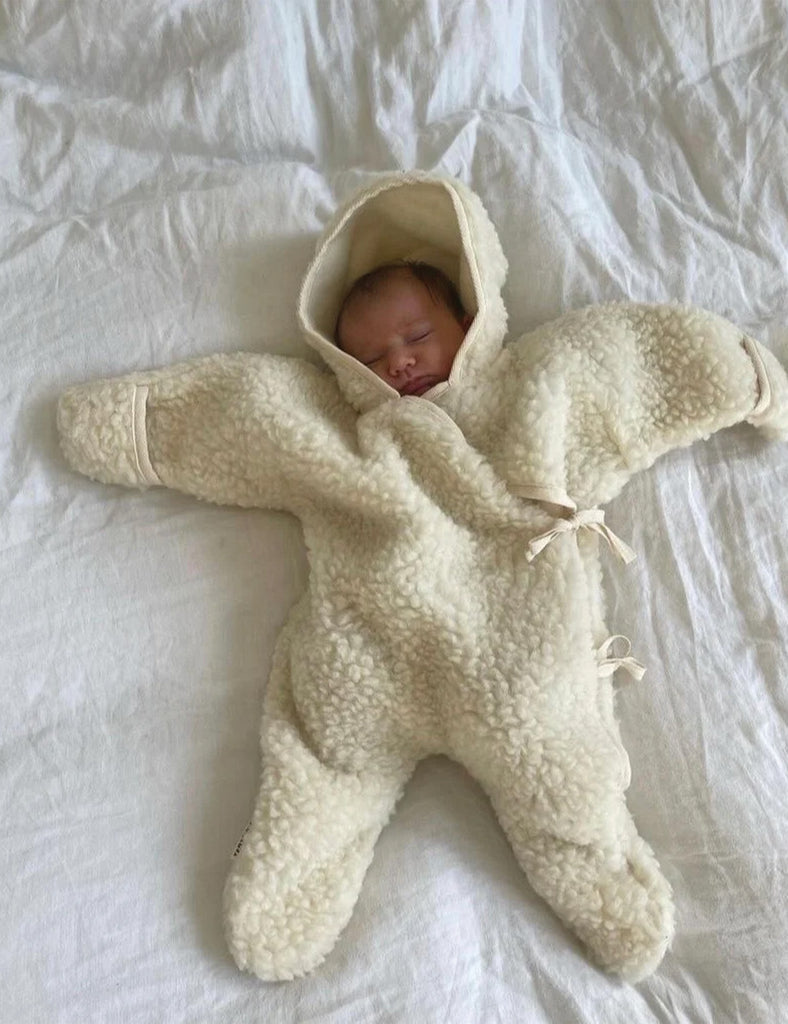 Newborn baby in a cream-colored fleece onesie lying on a white surface