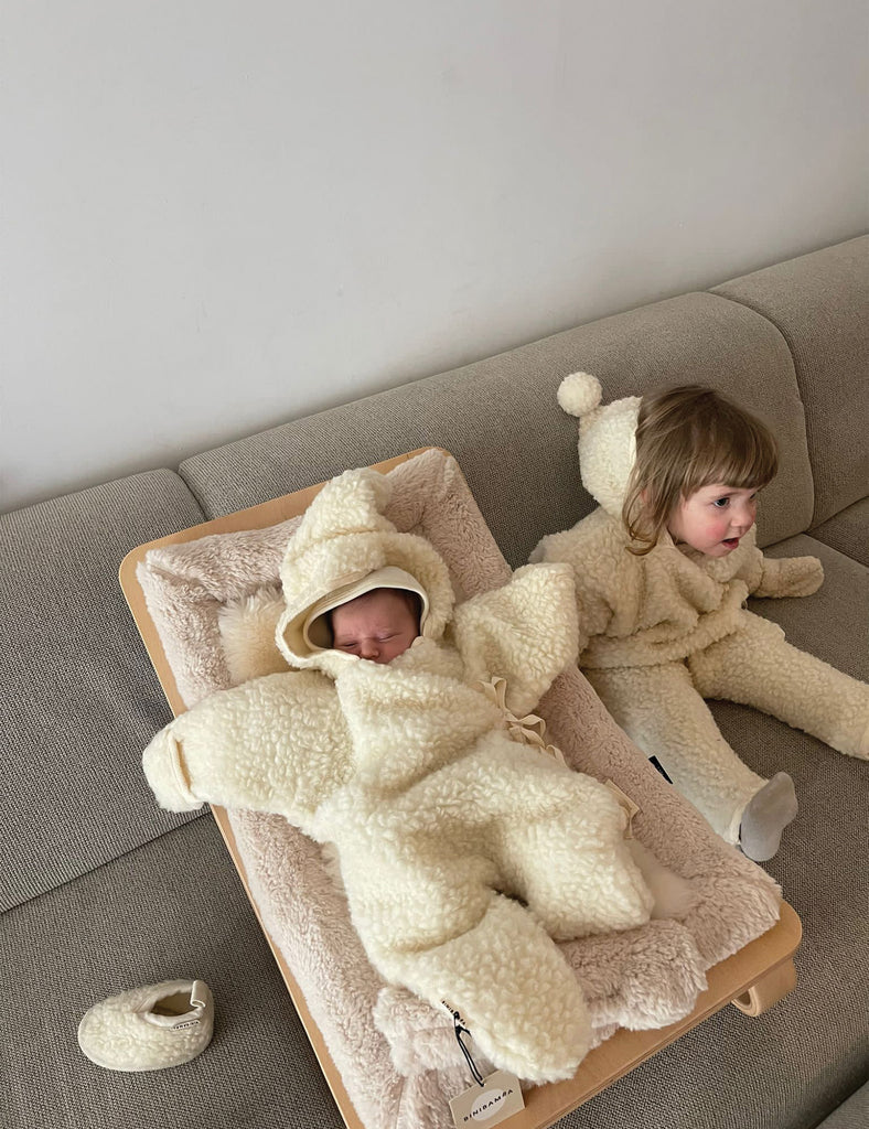 Two children in fluffy bear-themed outfits on a couch and wooden tray.
