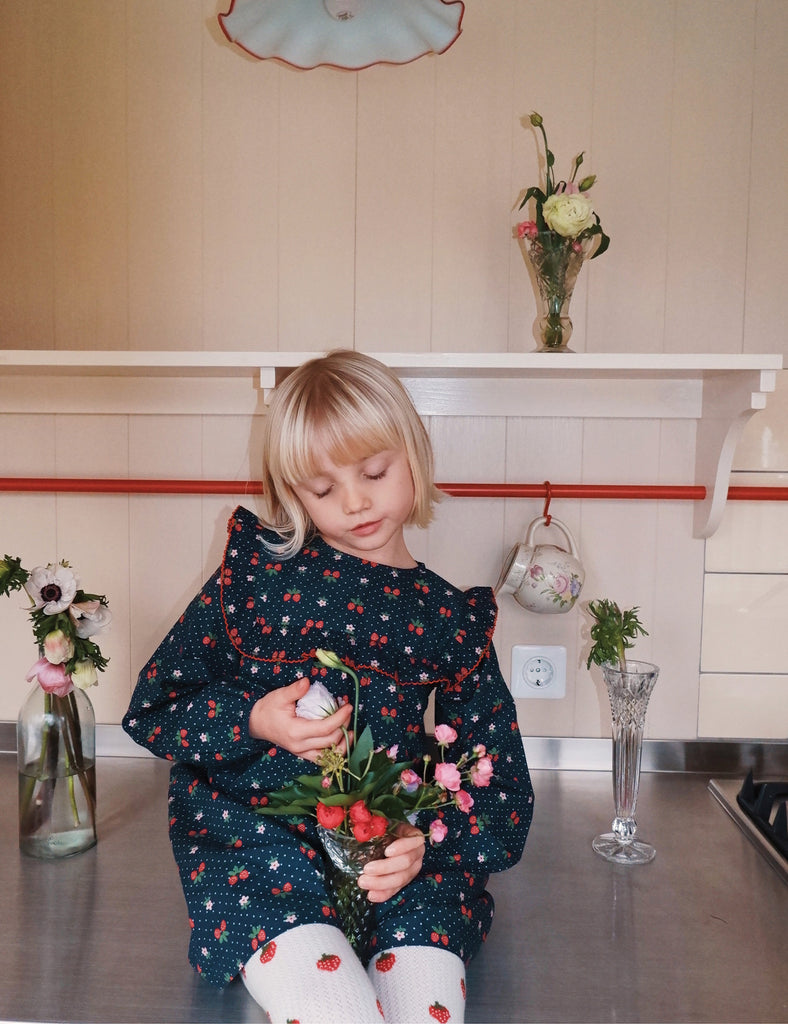 Child in a floral outfit holding flowers in a kitchen setting