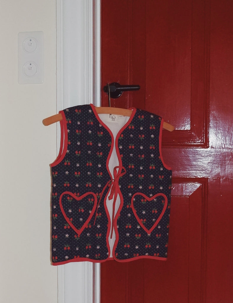 Children's vest with heart designs on a hanger against a red door.