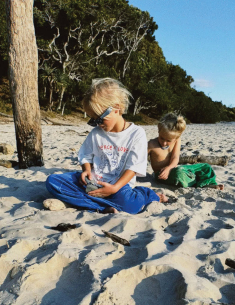 Two children playing on a sandy beach with trees and clear sky in the background.
