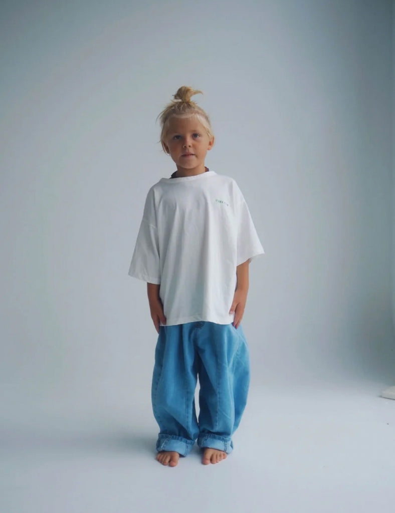 Child wearing a white t-shirt and blue pants against a plain background