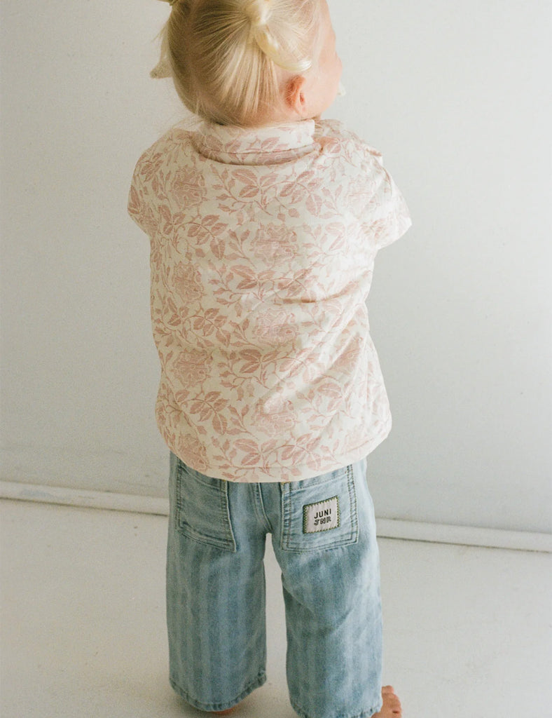 Child wearing a floral shirt and jeans against a plain background